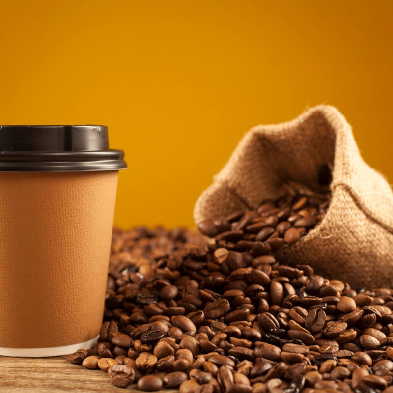 A compostable coffee cups next to coffee beans.