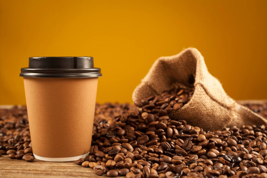 A compostable coffee cups next to coffee beans.